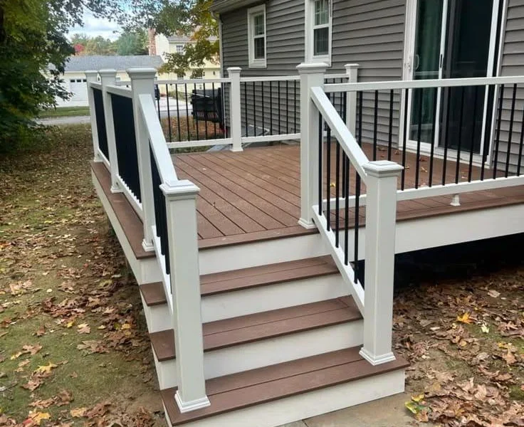Brown composite deck and stairs with white railing posts and black balusters