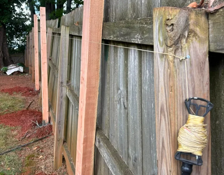 New wood post set along an old privacy fence during a fence repair