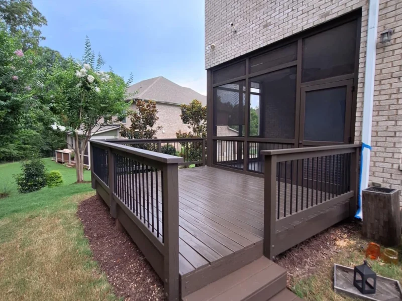 Brown stained deck with black balusters and stairs beside a brick house